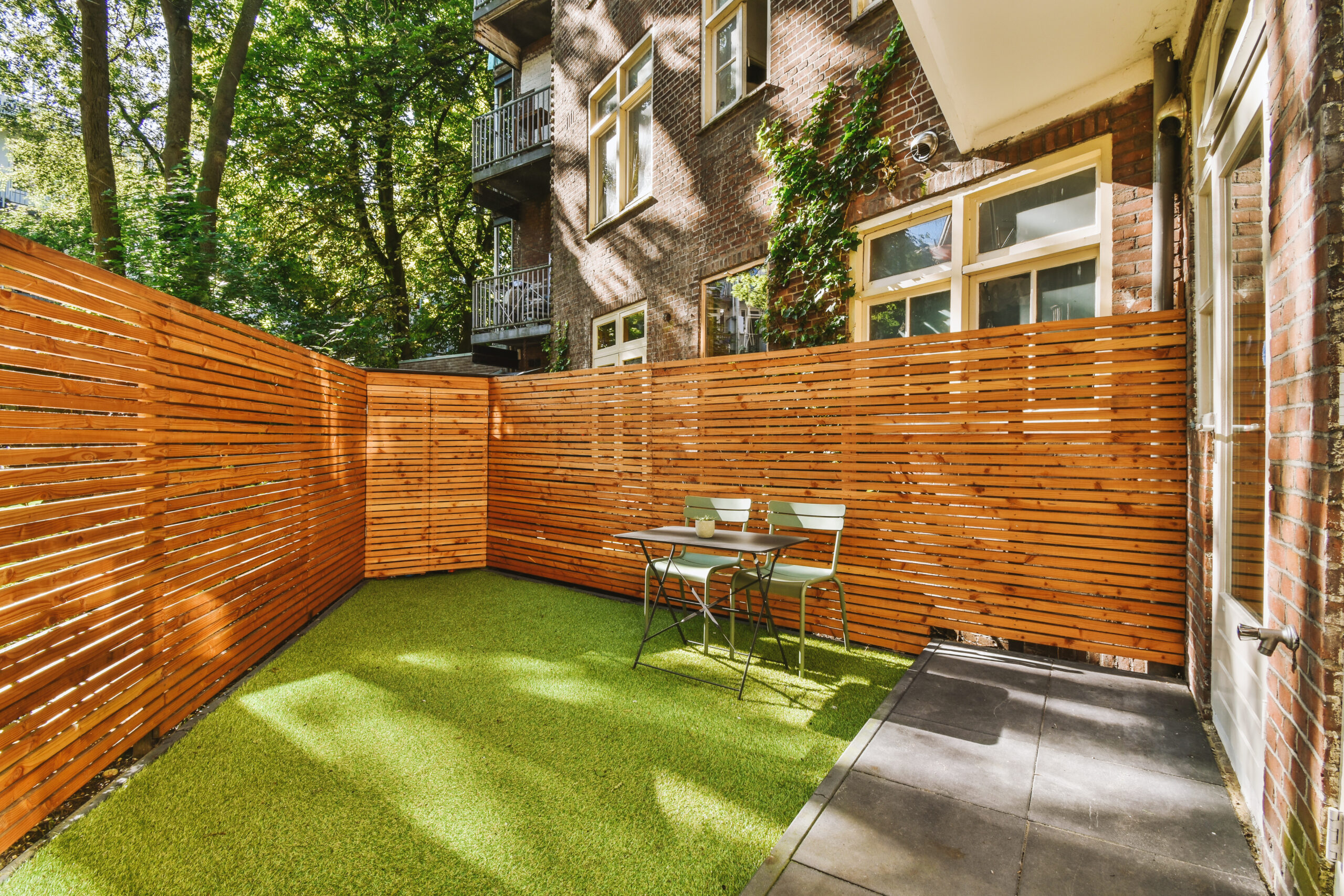 Neat paved patio with sitting area and small garden near wooden fence