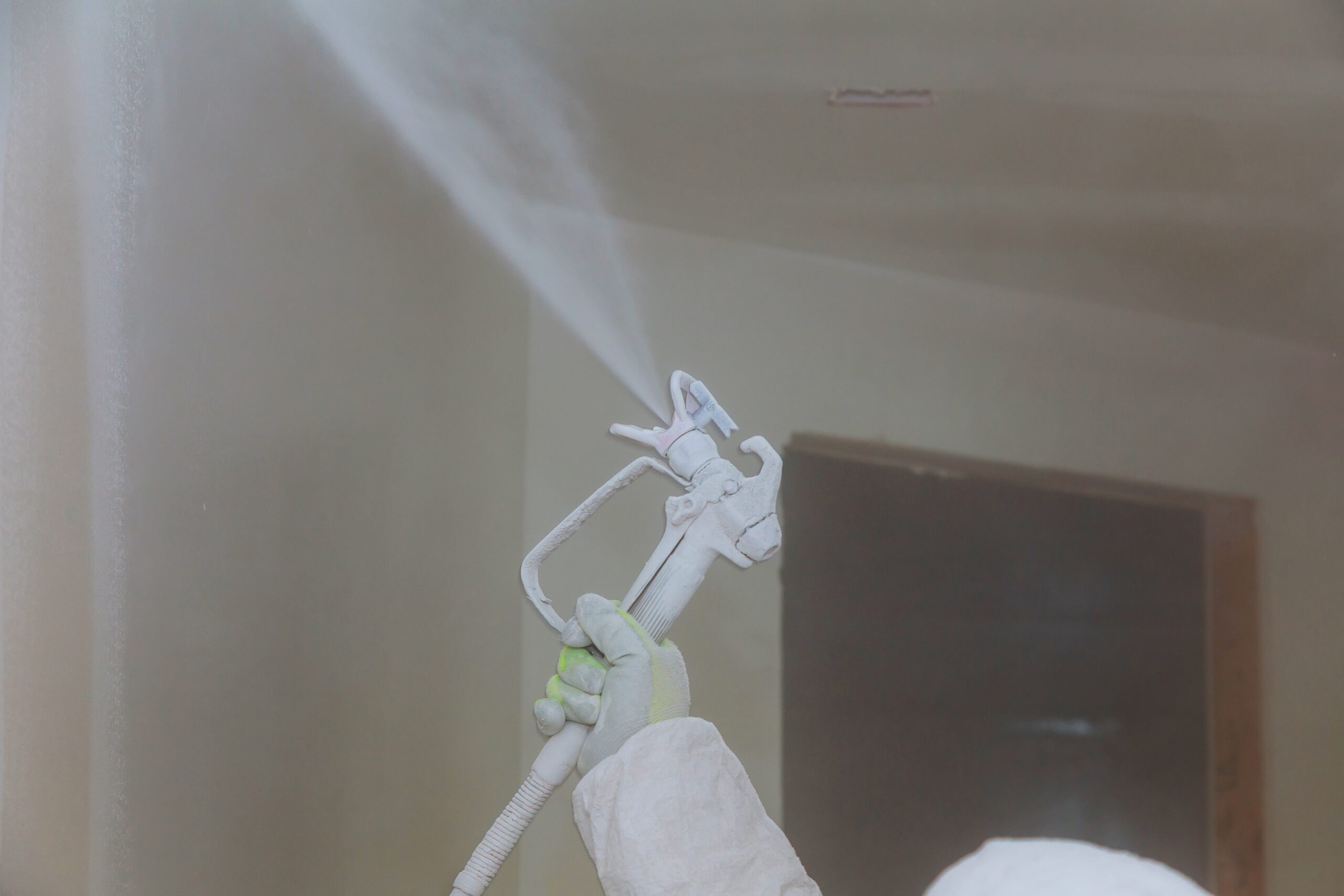 Worker painting wall with spray gun in white color. House Painter Spray