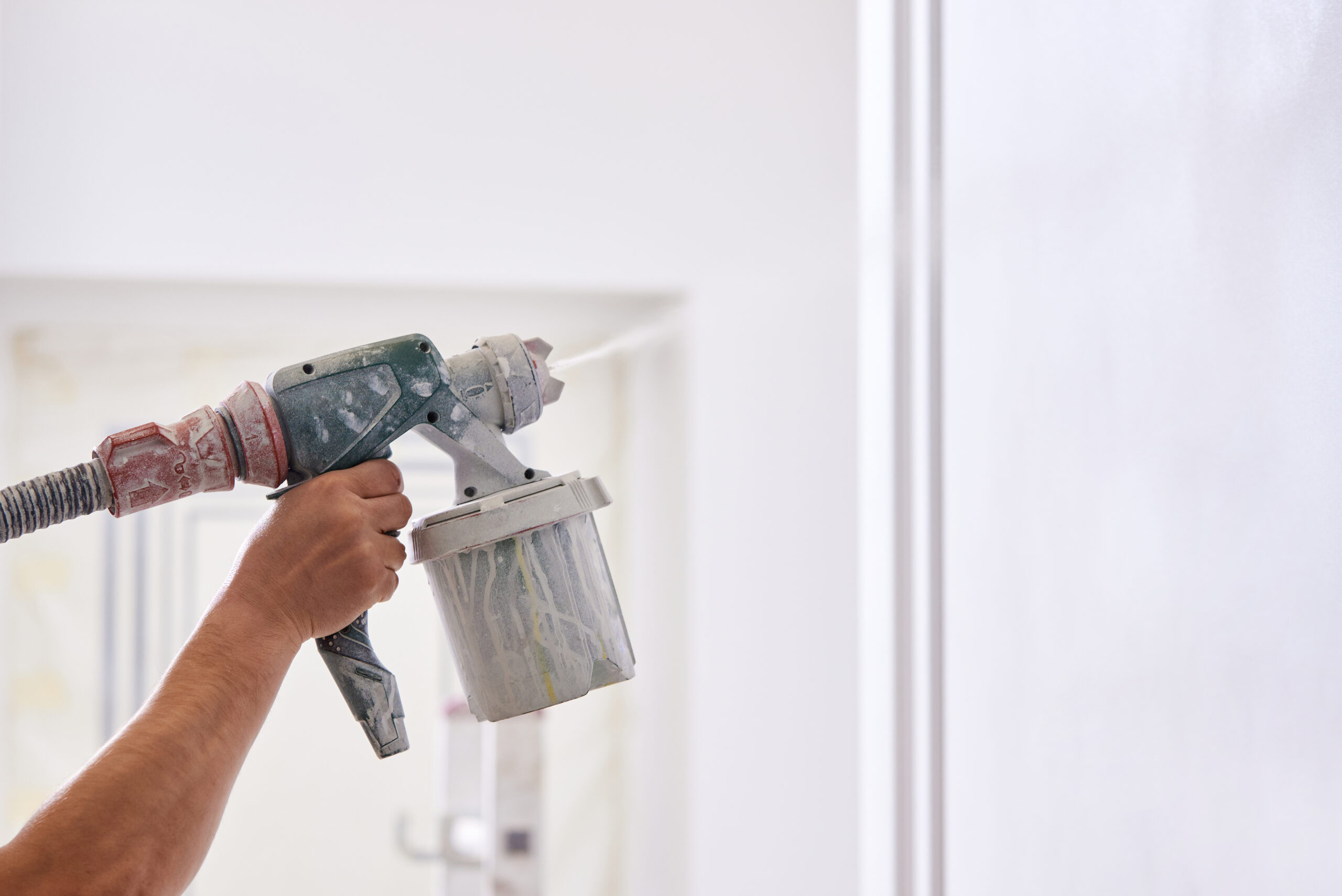 Condtruction worker painting wall with spray gun in white color.